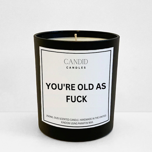 Funny candle with white label saying "You're Old As Fuck" on black jar
